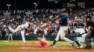 Baseball players in an intense MLB game under stadium lights with fans in the background.
