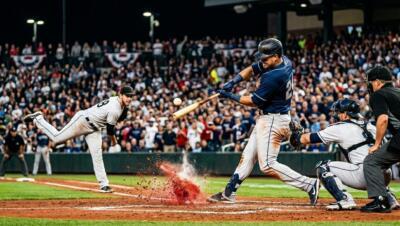 Baseball players in an intense MLB game under stadium lights with fans in the background.