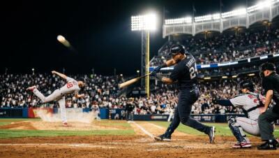Baseball players in a tense MLB matchup under stadium lights as a batter connects with a pitch.